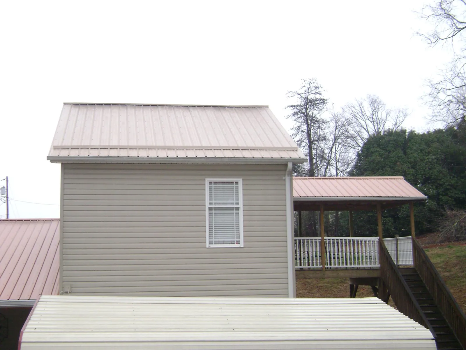 Tan metal roofs on a two story addition and attached porch, from a Roof Replacement job in Roscoe